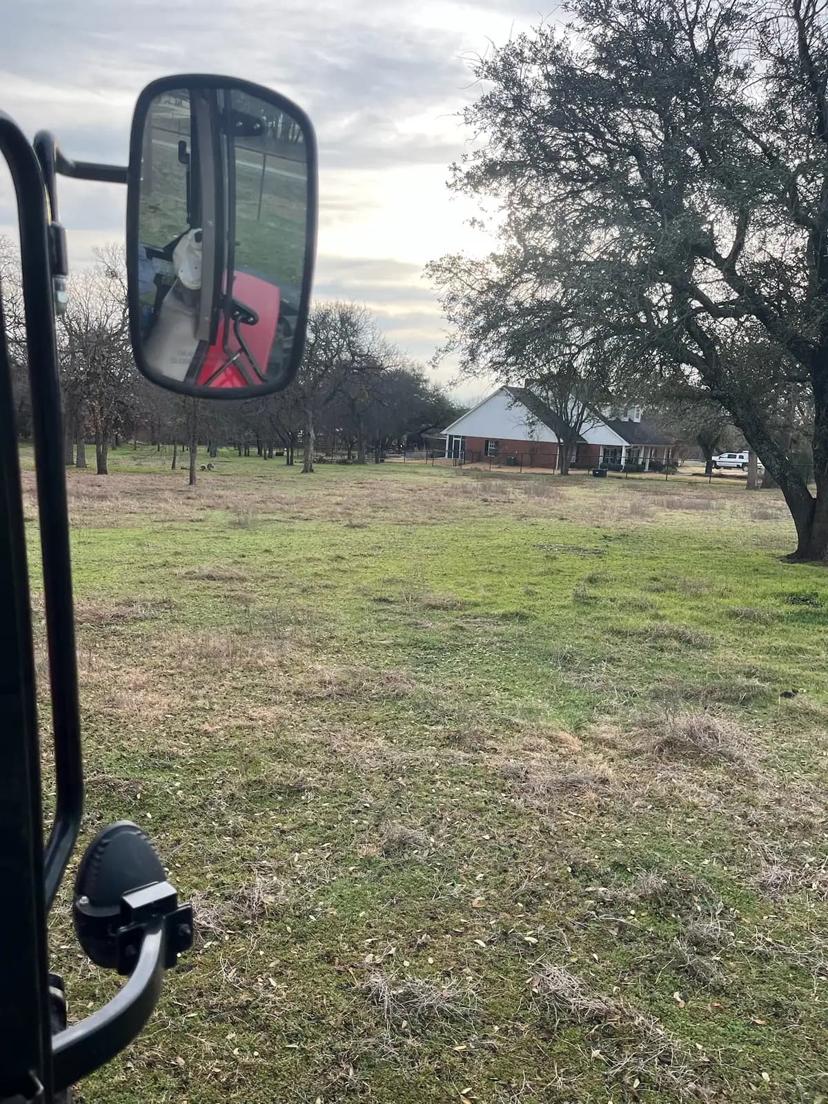 Brush hog mowing a pasture under mature oaks with a red tractor near Granbury, TX